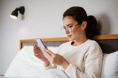 Evde kötü otururken cep telefonu kullanan güzel bir kız.
