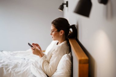 Evde kötü otururken cep telefonu kullanan güzel, ciddi bir kız.