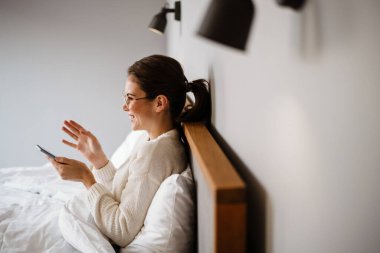 Güzel neşeli kız evde kötü otururken cep telefonu kullanıyor ve gülümsüyor.