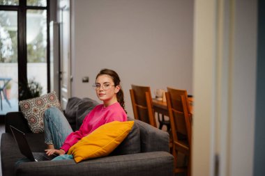 Evdeki kanepede otururken dizüstü bilgisayarla çalışan güzel kız.