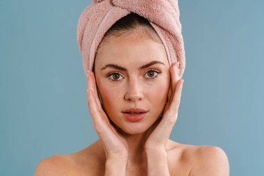 Havlu giymiş, mavi arka plandan izole edilmiş kameraya bakan çekici üstsüz kız.