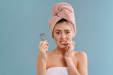 Kirpik bigudiyle poz veren, mavi arka planda saklanmış, korkmuş, güzel bir kız.