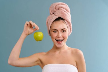 Havlu giyen, gülümseyen ve elmayla poz veren mutlu bir kız.