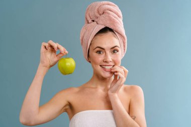 Havlu giyen, gülümseyen ve elmayla poz veren mutlu bir kız.