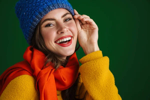 美しいです幸せな女の子で暖かいです帽子とスカーフ笑顔でカメラ隔離されました上の緑の背景 — ストック写真