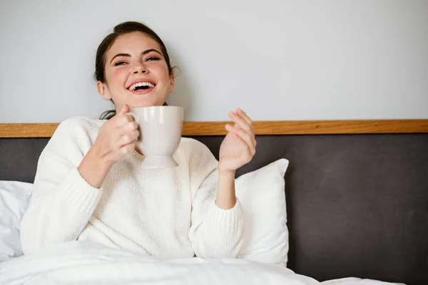 迷人而快乐的女孩一边坐在家里一边笑 一边喝咖啡 — 图库照片