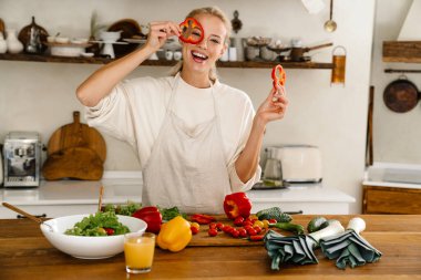 Güzel, mutlu bir kadın, sıcak mutfakta yemek pişirirken sebzelerle dalga geçiyor.