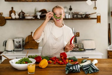Güzel, mutlu bir kadın, sıcak mutfakta yemek pişirirken sebzelerle dalga geçiyor.