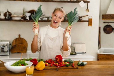 Güzel, neşeli bir kadın, sıcak mutfakta yemek pişirirken pırasalarla dalga geçiyor.