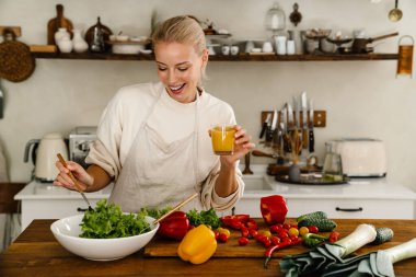 Güzel, mutlu bir kadın. Mutfakta yemek yaparken gülümsüyor ve meyve suyu içiyor.