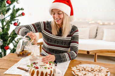 Noel Baba şapkalı mutlu bir kadın Noel 'i evde pasta ve çam ağacıyla kutluyor.