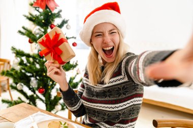 Mutlu güzel bir kız Noel yemeğini evde yerken hediye olarak fotoğraf çekiyor.