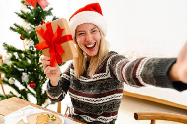 Mutlu güzel kız evde Noel yemeği yerken hediyeyle fotoğraf çekiyor.