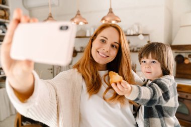 Oğluyla cep telefonuyla selfie çeken mutlu bir annenin resmi.