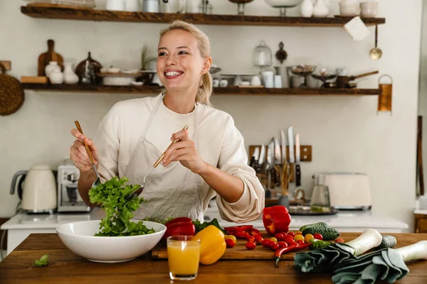 아름다운 여인이 미소짓고 샐러드를 준비하면서 주방에서 점심을 만드는 — 스톡 사진