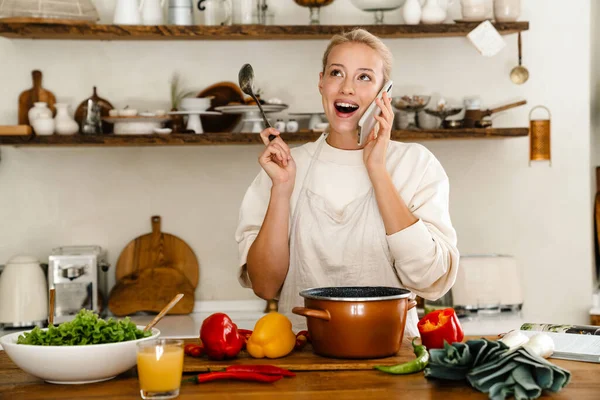 Mulher Surpresa Bonita Falando Celular Enquanto Faz Almoço Cozinha Acolhedora — Fotografia de Stock