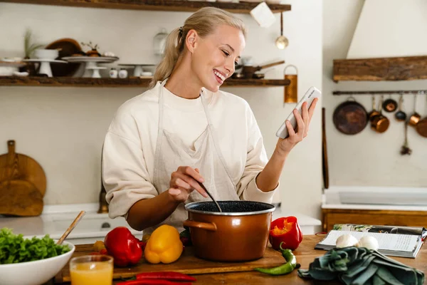 Güzel Neşeli Bir Kadın Mutfakta Yemek Yaparken Gülümsüyor Cep Telefonu — Stok fotoğraf