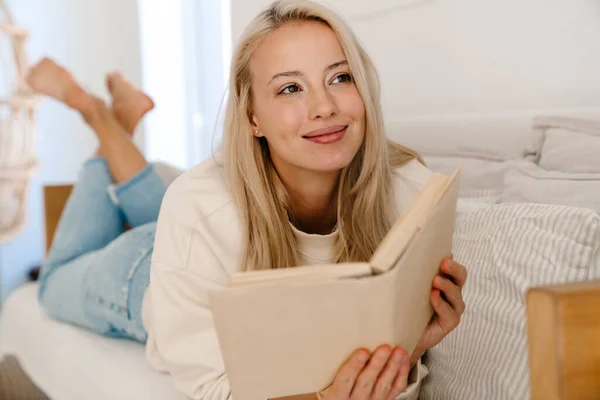 美しい陽気な女性笑顔と読書本ながら横たわっソファに居心地の良い部屋 — ストック写真