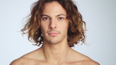 Hoşnutsuz bir adam kafasını sallıyor. Stüdyodaki beyaz duvarın üzerinde tek başına duruyor.