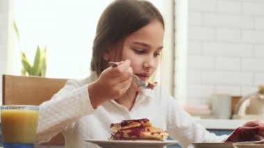 Evde kahvaltı yapan pozitif kız çocuğu cep telefonuyla video seyrediyor.