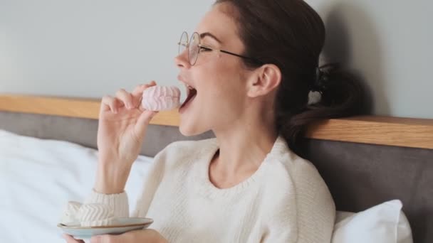 Jong Positief Meisje Ligt Bed Eten Marshmallow Binnen Thuis — Stockvideo