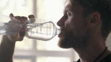 Sarışın, kaslı bir adamın yakın çekim görüntüsü stüdyoda su içiyor.