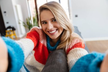 Güzel genç bir kadın evde kanepede otururken selfie çekiyor ve gülümsüyor.