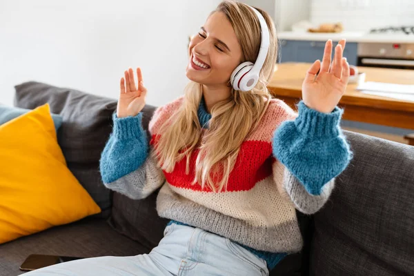 快乐的年轻女子坐在沙发上 用耳机听音乐 — 图库照片