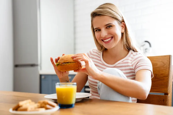 Mujer Joven Sonriente Comiendo Hamburguesa Cocina Casa — Foto de Stock