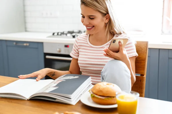 Mujer Joven Sonriente Leyendo Revista Mientras Está Sentada Cocina Comiendo — Foto de Stock