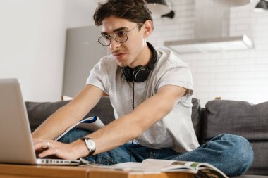 Evde dizüstü bilgisayar kullanan yakışıklı bir adamın fotoğrafı.