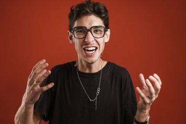 Kızgın genç hippi, elleri kırmızı arka planda izole bir şekilde el kol hareketi yapıyor.