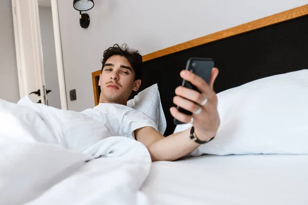 Imagen Hombre Guapo Encuentra Cama Uso Teléfono Móvil Interior Casa —  Fotos de Stock