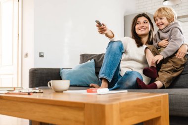 Genç ve mutlu bir kadının oğluyla evde televizyon izlediği görüntüsü.