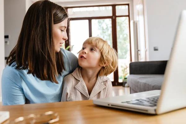 照片上的年轻而积极的漂亮女人和她的儿子一起在家里用笔记本电脑 — 图库照片