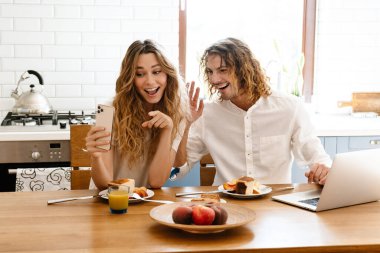 Keyifli, güzel bir çift. Mutfakta kahvaltı ederken cep telefonu ve laptop kullanıyorlar.