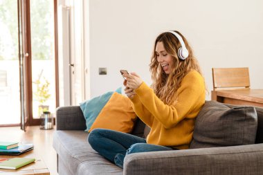 Evdeki kanepede dinlenirken kulaklık takan neşeli, güzel kız.