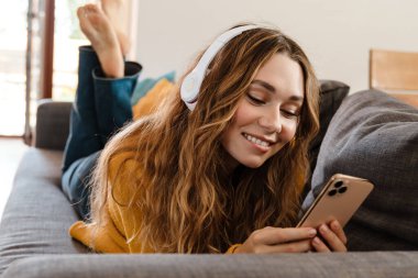 Evdeki kanepede yatarken kulaklık takan neşeli, güzel bir kız.