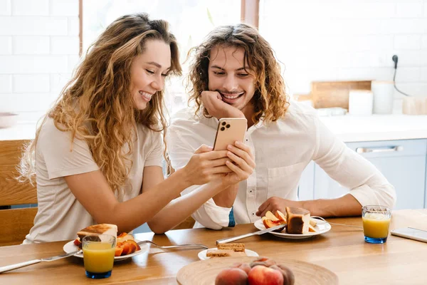 Feliz Hermosa Pareja Sonriendo Utilizando Teléfono Celular Mientras Desayuna Acogedora — Foto de Stock