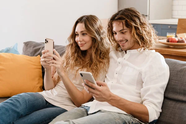 幸福的年轻夫妇一边笑着 一边用手机在沙发上休息 — 图库照片