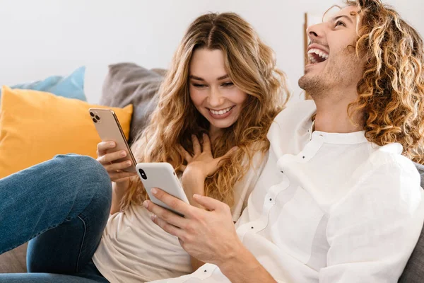 Entzücktes Schönes Paar Lacht Und Benutzt Mobiltelefone Während Sich Hause — Stockfoto