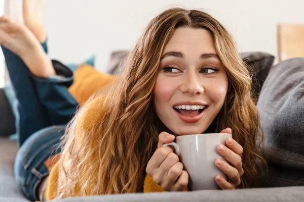 Gioioso Bella Ragazza Sorridente Bere Mentre Sdraiato Sul Divano Casa — Foto Stock