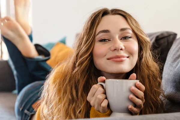 Gioioso Bella Ragazza Sorridente Bere Mentre Sdraiato Sul Divano Casa — Foto Stock