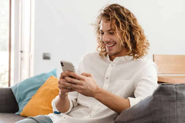 Glad Stilig Kille Ler Och Använder Mobiltelefon Medan Vilar Soffan — Stockfoto