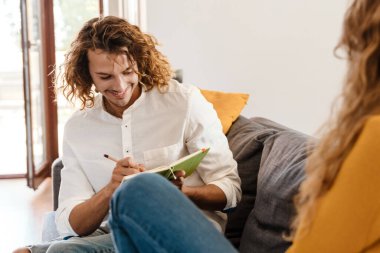 Evdeki kanepede otururken kız arkadaşının portresini çizen mutlu yakışıklı adam.