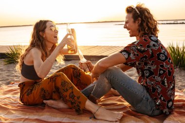 Sahilde bira içen mutlu, genç bir çiftin görüntüsü.