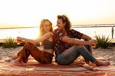 Sahilde bira içen mutlu, genç bir çiftin görüntüsü.