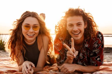 Kumsalda uzanıp barış jesti yapan mutlu bir çiftin görüntüsü.