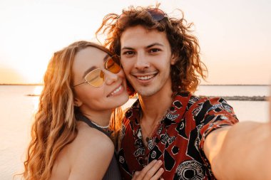 Kumsalda fotoğraf çeken mutlu, genç bir çiftin görüntüsü.