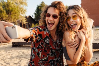 Sahilde cep telefonuyla selfie çeken heyecanlı genç bir çift.